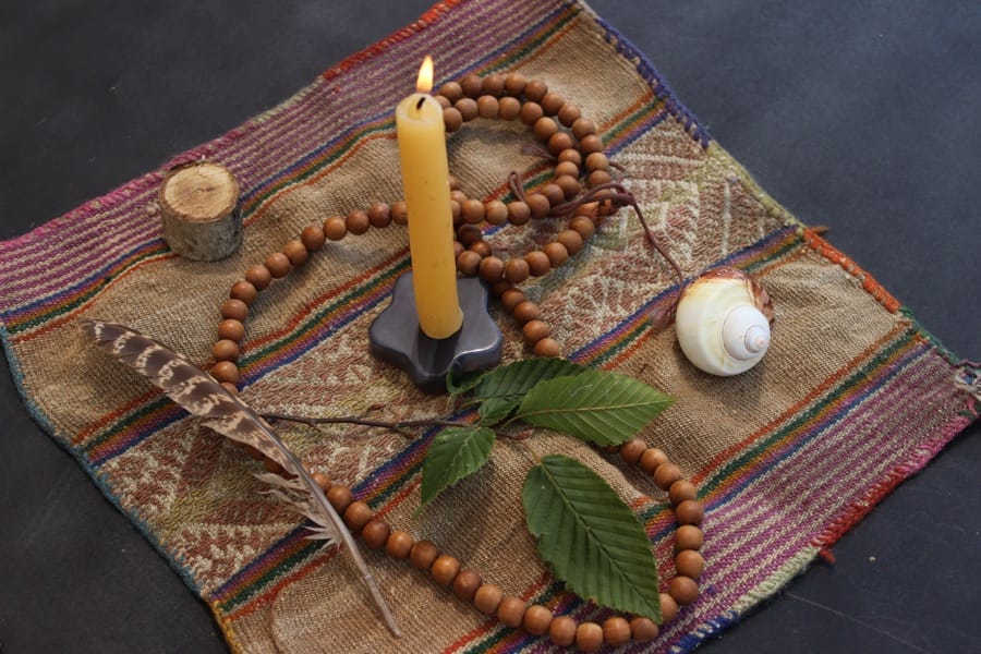 A sacred altar with candle, mala beads, feather, and shell